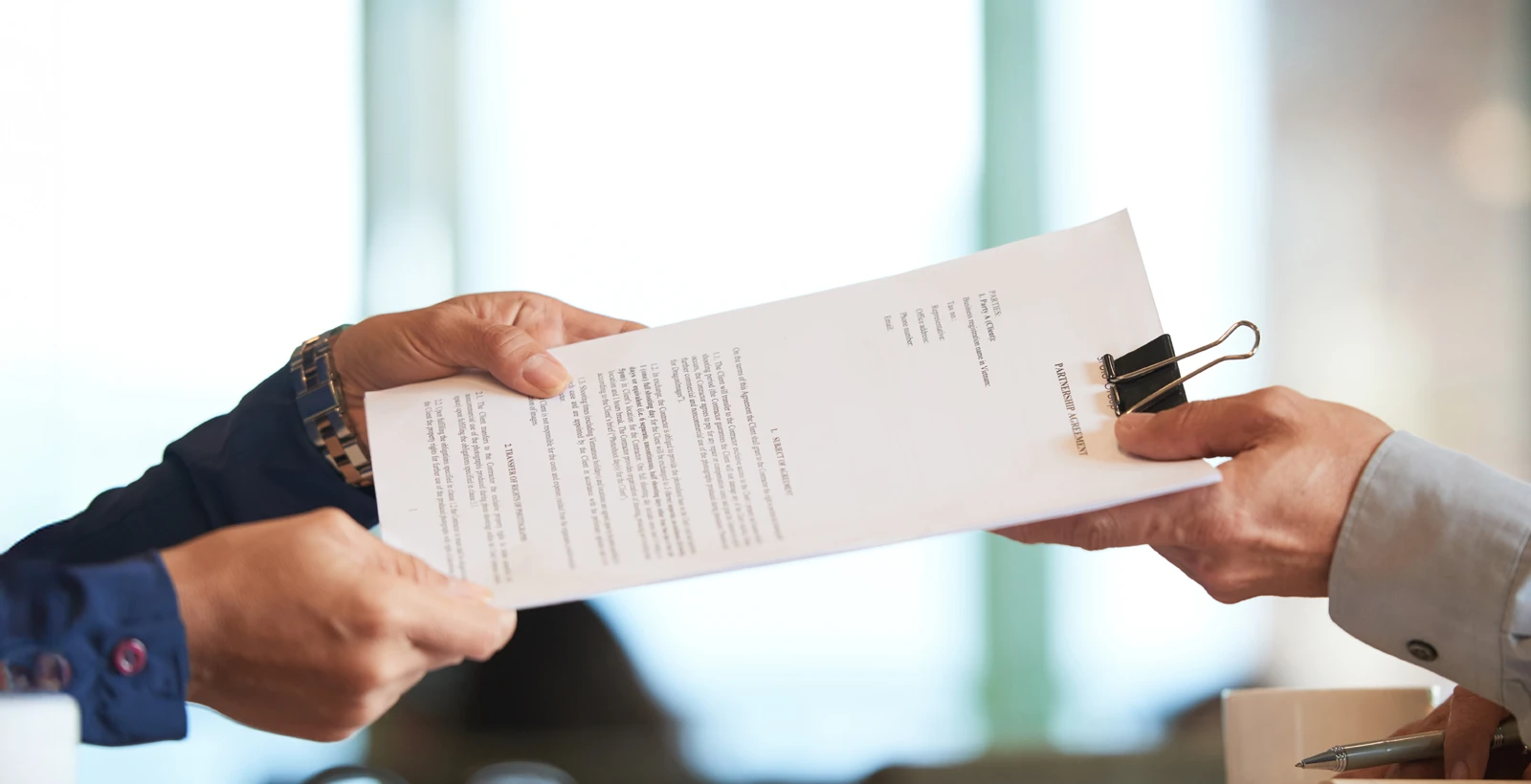 Two professionals exchanging a document with a binder clip, symbolizing agreements and compliance costs