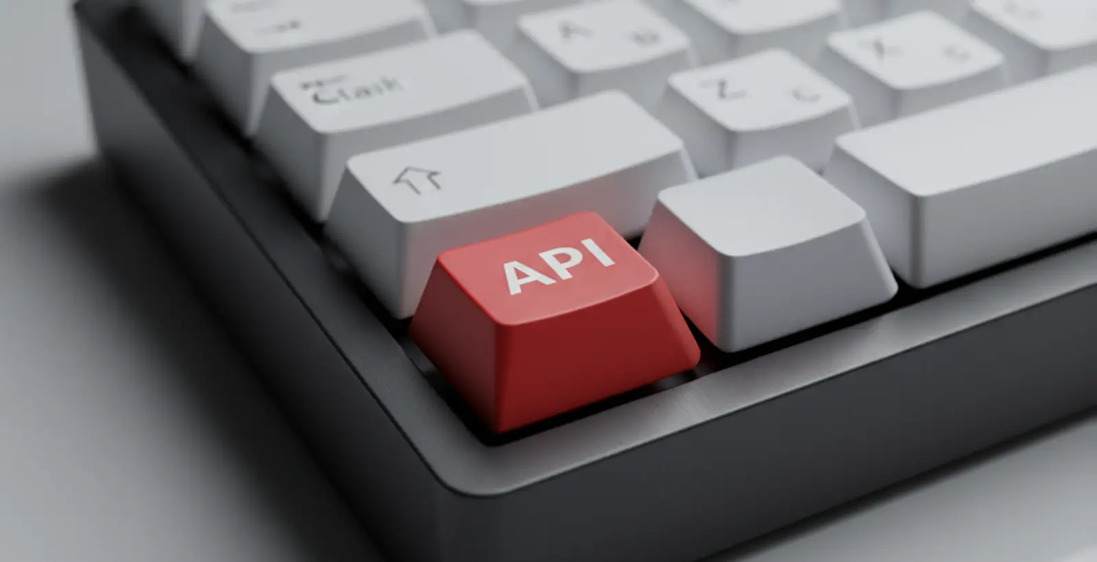 Hyper-realistic close-up of a modern PC keyboard, all keys matte white and minimal; one key is bright red with 'API' in crisp white text, symbolizing API focus for web application penetration testing services on API-driven platforms, with sharp lighting and a clean, studio background.
