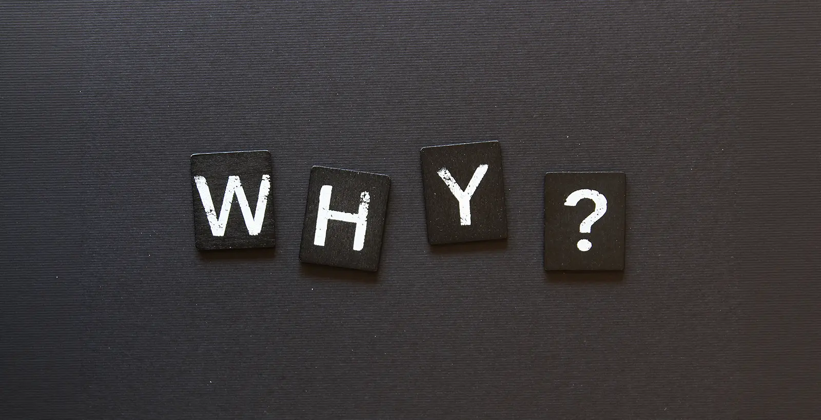 Black wooden tiles spelling 'WHY?' on a dark textured background, symbolizing the investigation into common reasons organizations fail HITRUST validation